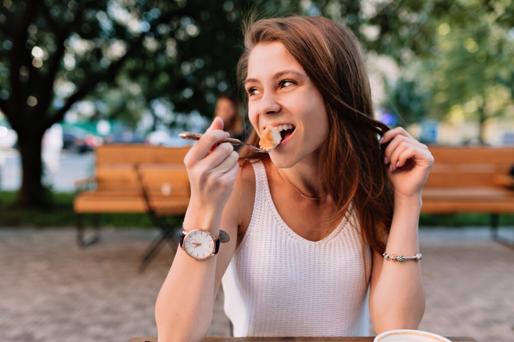 Does Chewing Food Well Help Digestion? 5 Eating Habits Improvement 2 smiling caucasian female model eating fancy cupcake outdoor summer cafeteria